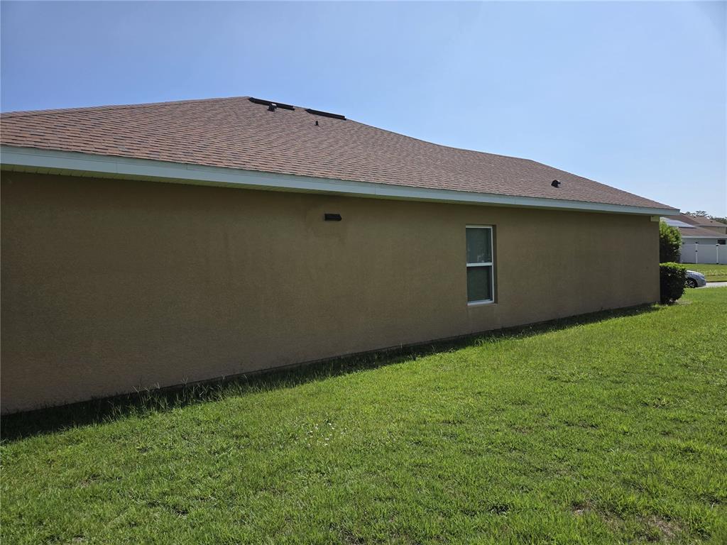 The exterior side view of a tan stucco house features a single window and roof — 2280 SHEBOYGAN PLACE, KISSIMMEE, FL