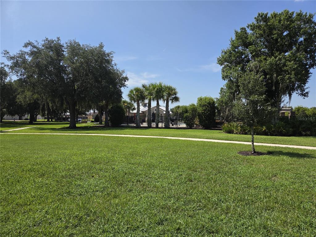 A grassy park area features a paved walking path, mature trees, and a fenced pool — 2280 SHEBOYGAN PLACE, KISSIMMEE, FL