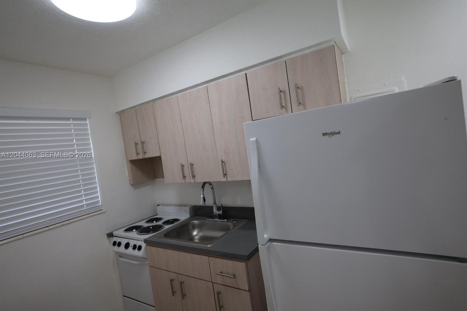 A small kitchen features light wood cabinets, a white stove, a sink, and a refrigerator — 1235 W 66th St # 13, Hialeah FL 33012, HIALEAH, FL