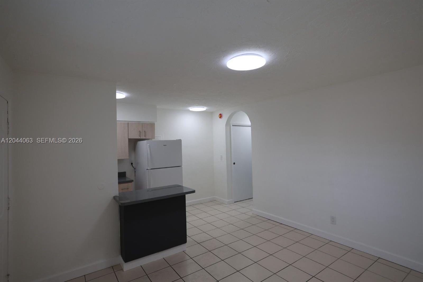 A kitchen with a breakfast bar, white refrigerator, and tile flooring opens to a hallway — 1235 W 66th St # 13, Hialeah FL 33012, HIALEAH, FL