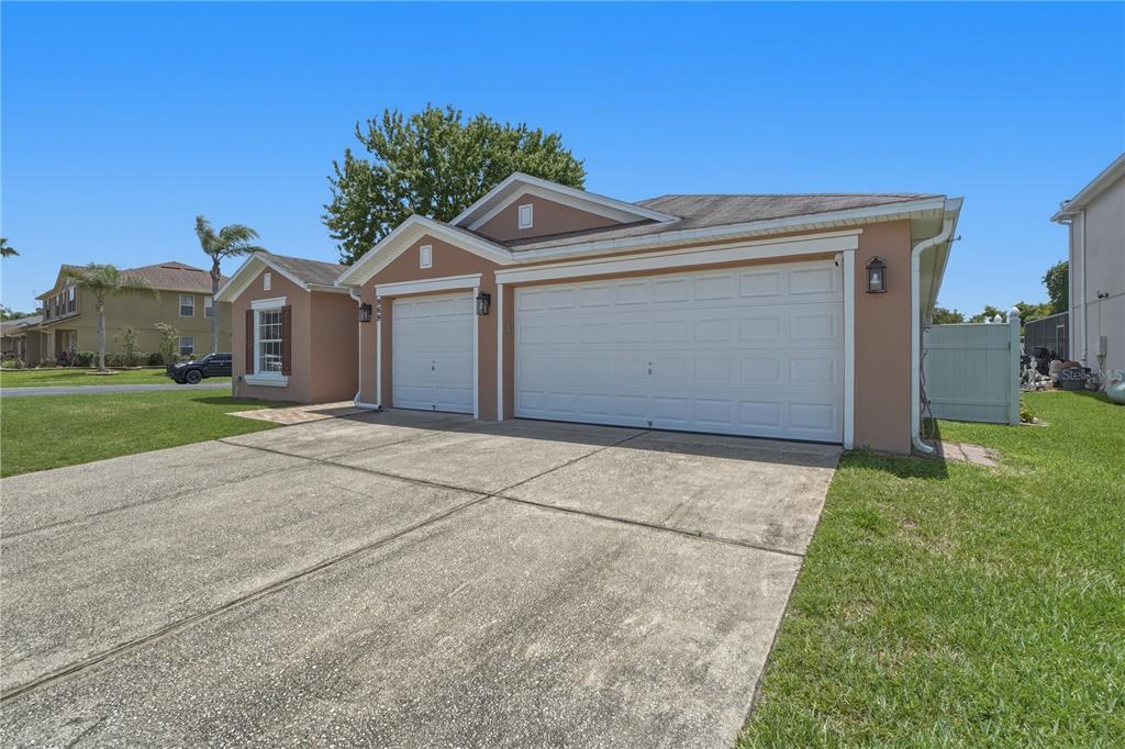 A tan house with a three-car garage and a concrete driveway under a blue sky — 969 HORSESHOE FALLS DRIVE, ORLANDO, FL