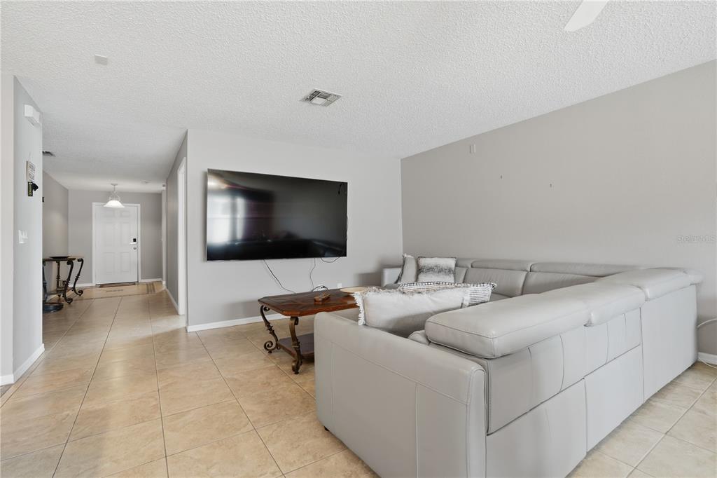 A living room features a large wall-mounted television, a sectional sofa, and tile flooring — 969 HORSESHOE FALLS DRIVE, ORLANDO, FL
