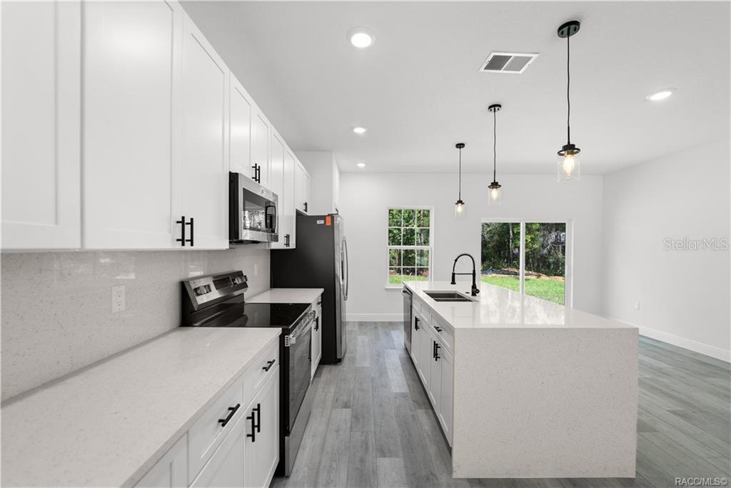 A modern kitchen features white cabinets, quartz countertops, stainless steel appliances, and a center island — 6097 N DARLINGTON DRIVE, CITRUS SPRINGS, FL