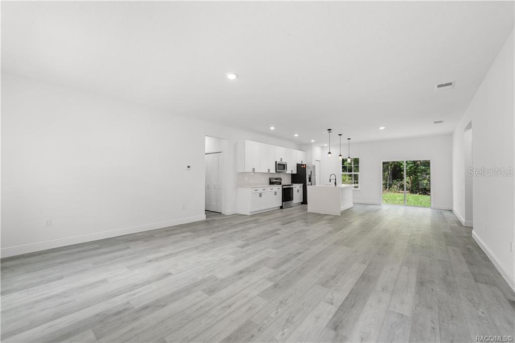 A bright, open-concept kitchen and living area features white cabinets and light wood-look flooring — 6097 N DARLINGTON DRIVE, CITRUS SPRINGS, FL