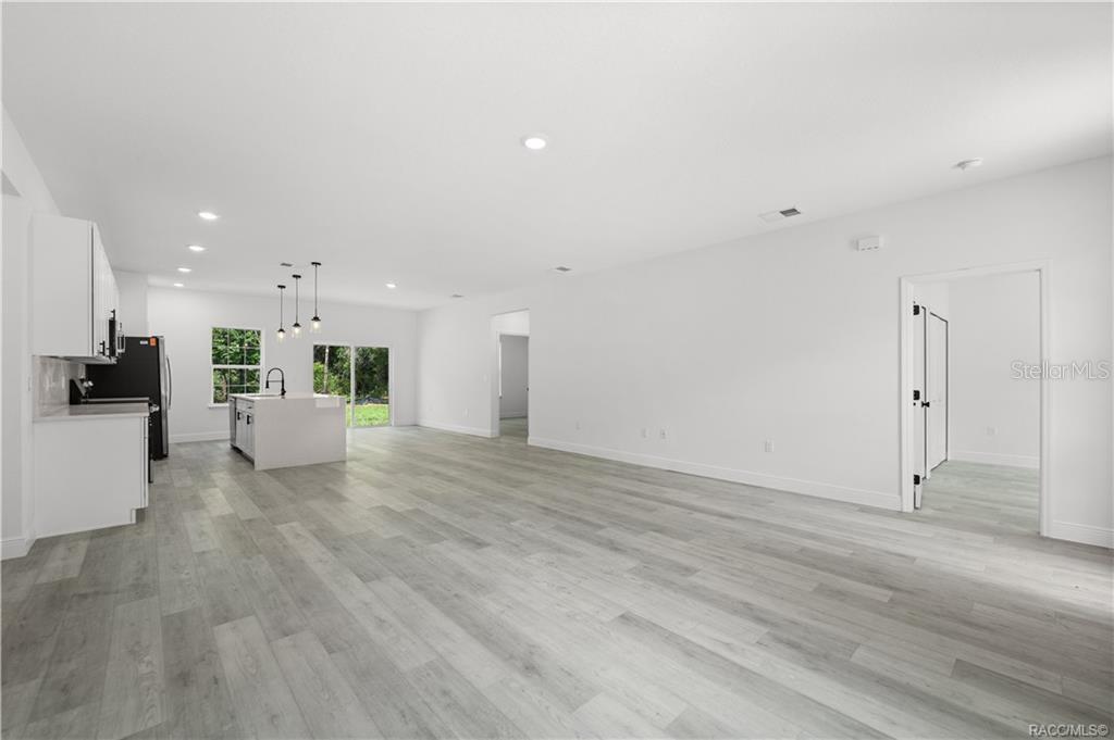 An open-concept kitchen and living area featuring white cabinetry, a center island, and wood-look flooring — 6097 N DARLINGTON DRIVE, CITRUS SPRINGS, FL