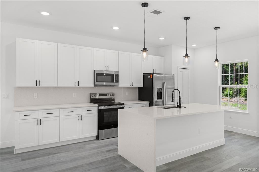 A modern kitchen features white cabinets, stainless steel appliances, a quartz island, and gray flooring — 6097 N DARLINGTON DRIVE, CITRUS SPRINGS, FL