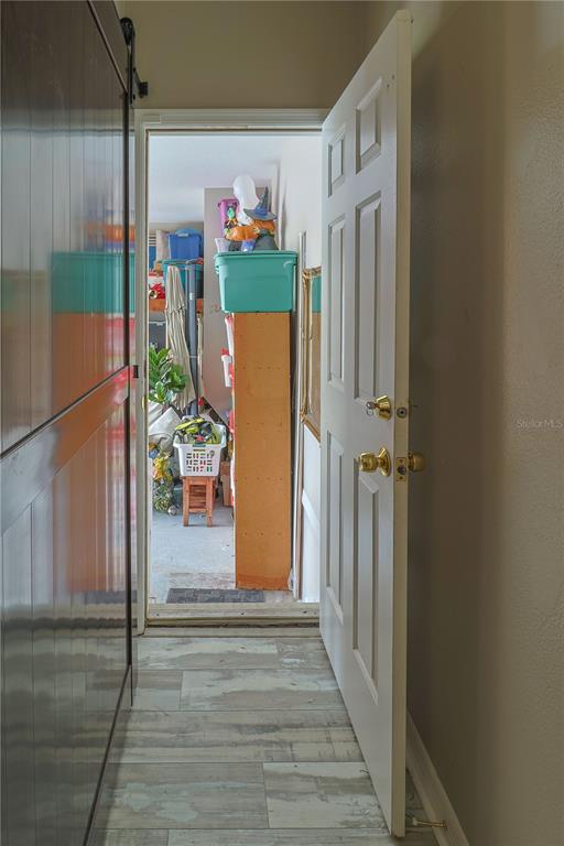 A white door opens into a cluttered garage with storage bins and a wooden shelf — 6244 SPOONBILL DRIVE, NEW PORT RICHEY, FL