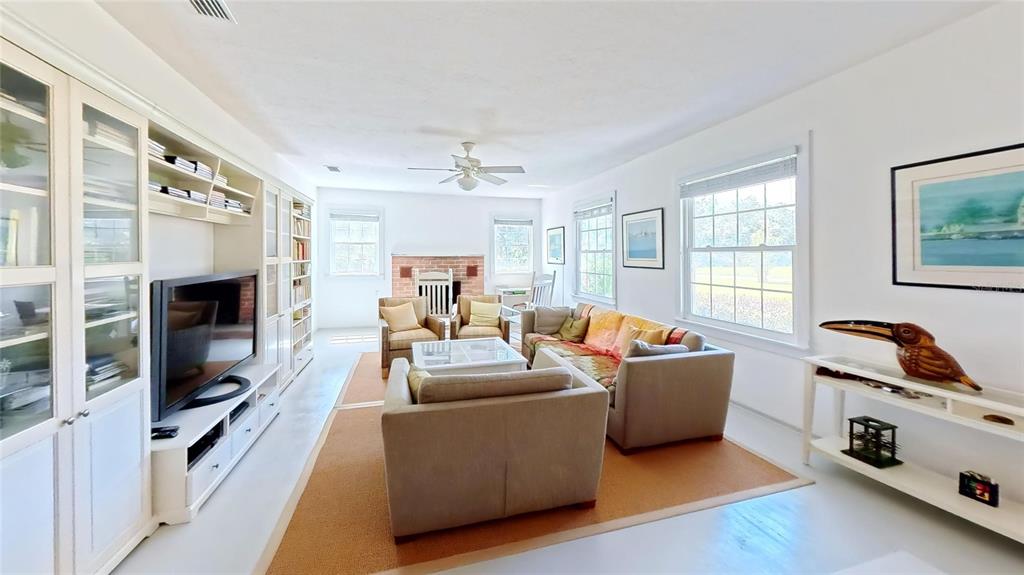A living room features a brick fireplace, built-in shelving, a television, and neutral furniture — 7390 180TH STREET, MC ALPIN, FL