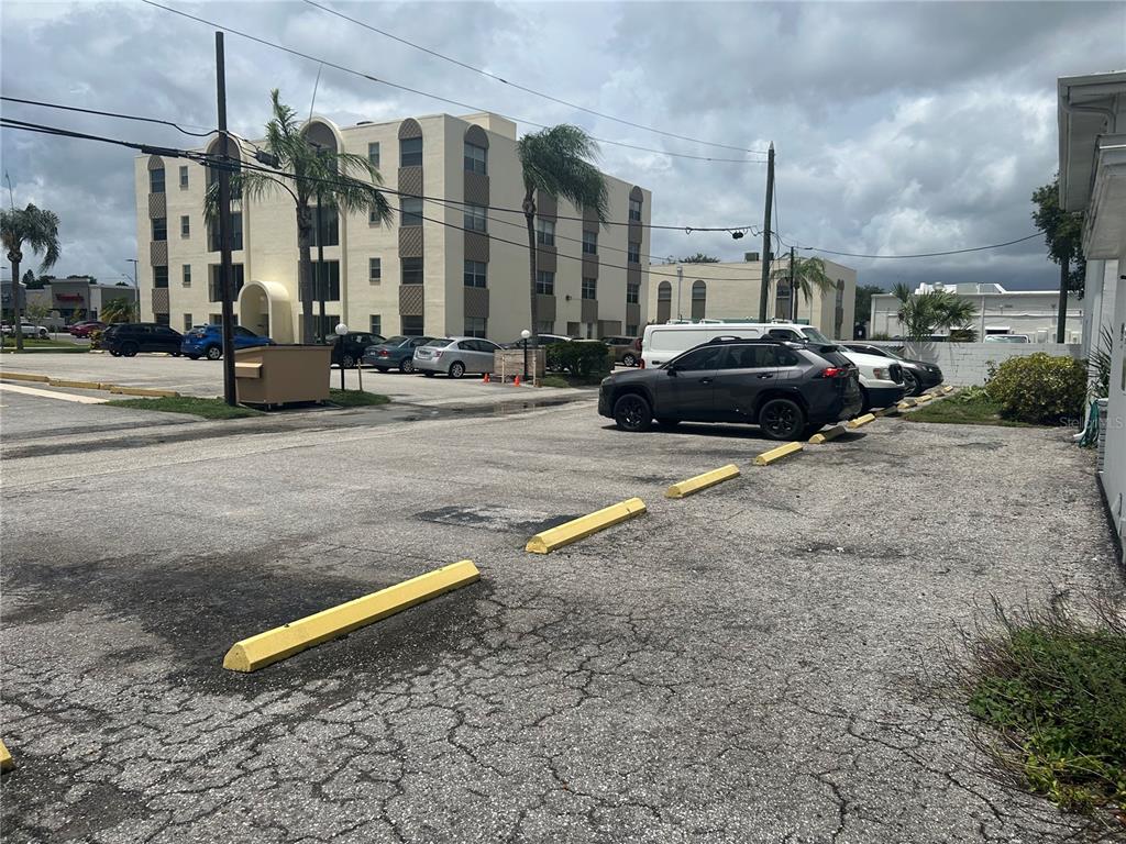 A parking lot with yellow concrete wheel stops sits in front of a multi-story building — 300 35TH AVENUE N UNIT F8, ST PETERSBURG, FL