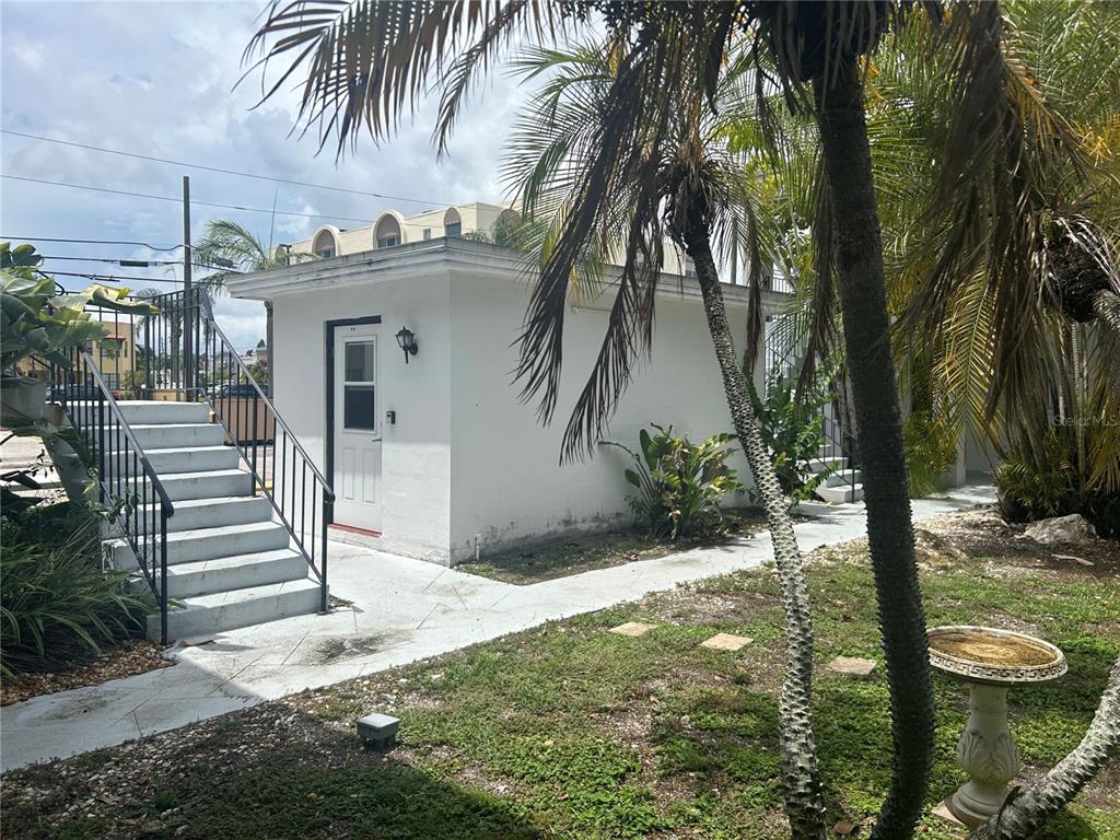A small white building with a door and stairs stands in a landscaped yard — 300 35TH AVENUE N UNIT F8, ST PETERSBURG, FL