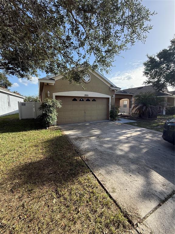 A tan single-story house features a two-car garage, a concrete driveway, and mature trees — 3201 SUMMER CRUISE DRIVE, VALRICO, FL