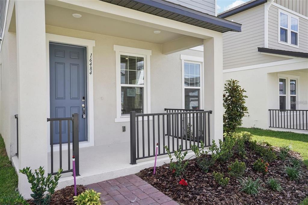A front porch with a blue door, metal railings, and a brick walkway — 16484 SILVER BROOK WAY, WINTER GARDEN, FL