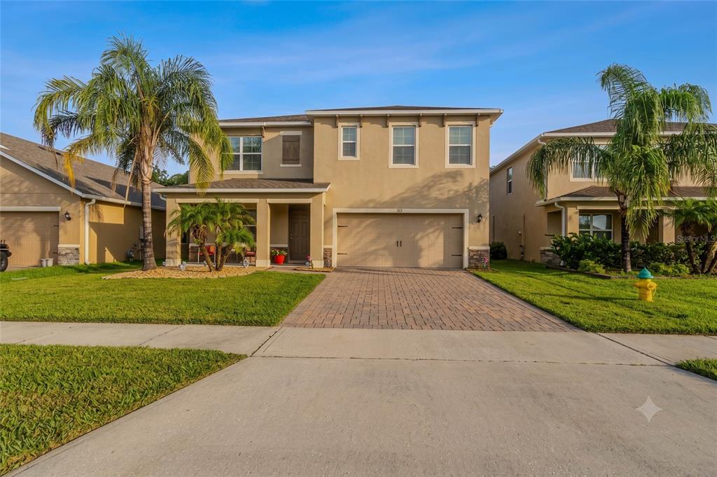 A two-story suburban house with a tan stucco exterior, a paved driveway, and palm trees — 247 LAZIO CIRCLE, DEBARY, FL