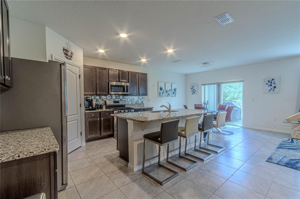 A kitchen with dark wood cabinets, granite countertops, and an island with three bar stools — 247 LAZIO CIRCLE, DEBARY, FL
