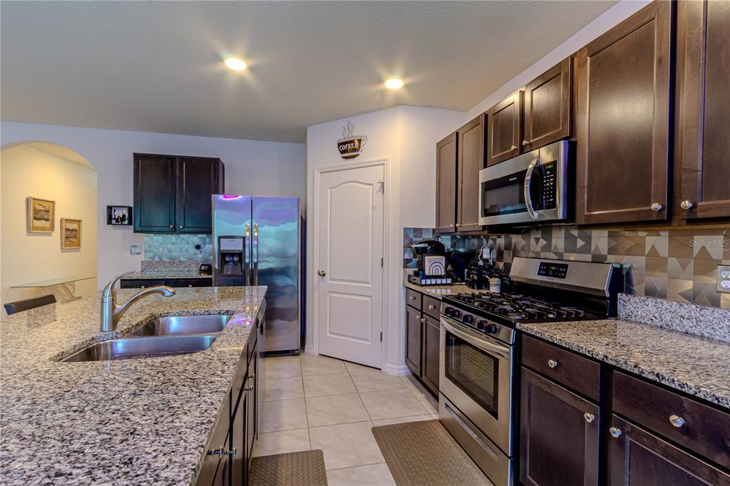 A kitchen features dark wood cabinets, granite countertops, stainless steel appliances, and a tiled backsplash — 247 LAZIO CIRCLE, DEBARY, FL