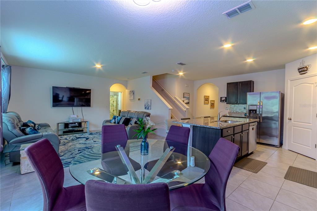 An open-concept living room and kitchen featuring a glass dining table and gray tile floors — 247 LAZIO CIRCLE, DEBARY, FL