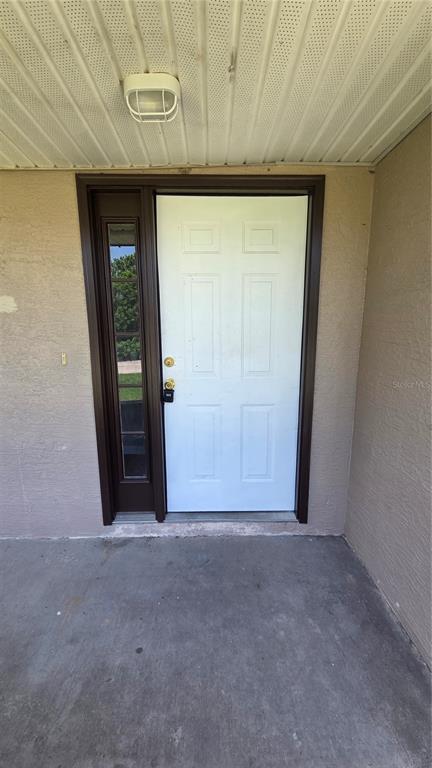 A white six-panel front door with a side window light sits under a covered porch — 1210 FAIRWAY DRIVE, LAKELAND, FL