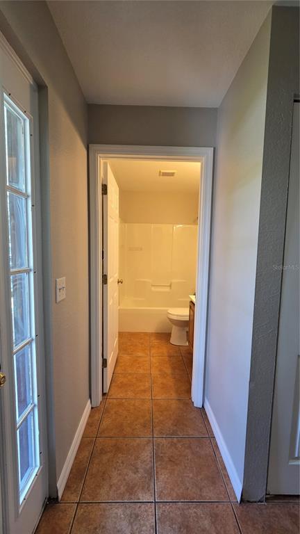A hallway with tile flooring leads to a bathroom featuring a tub and shower combination — 1210 FAIRWAY DRIVE, LAKELAND, FL