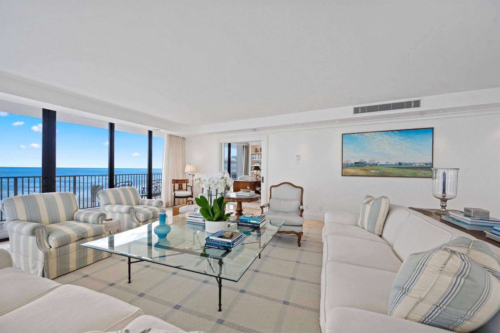 A bright living room features a glass coffee table, striped armchairs, and ocean views — 150 N Ocean Boulevard # 3, Palm Beach FL 33480, PALM BEACH, FL