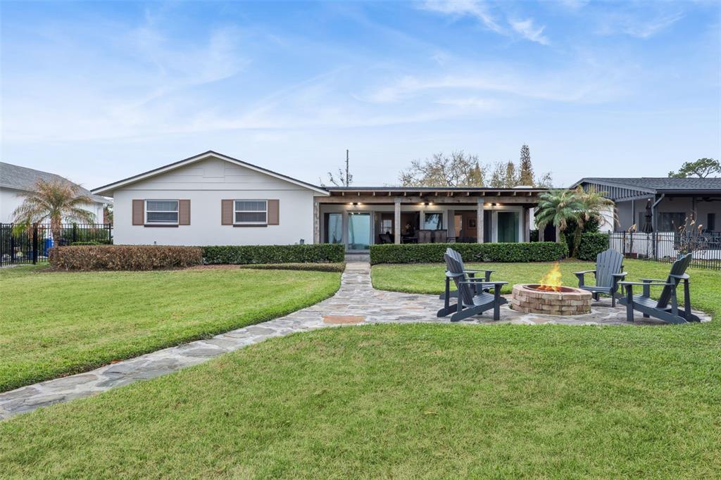 A backyard features a stone patio with a fire pit and chairs facing a house — 6007 LINNEAL BEACH DRIVE, APOPKA, FL