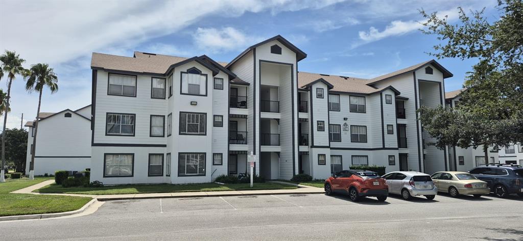 A three-story apartment building with white siding, dark trim, and a parking lot in front — 2207 ANTIGUA PLACE UNIT 715, KISSIMMEE, FL