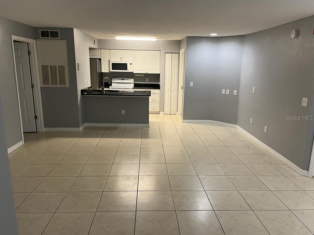An open-concept kitchen with white cabinets and a breakfast bar overlooks a tiled living area — 2207 ANTIGUA PLACE UNIT 715, KISSIMMEE, FL