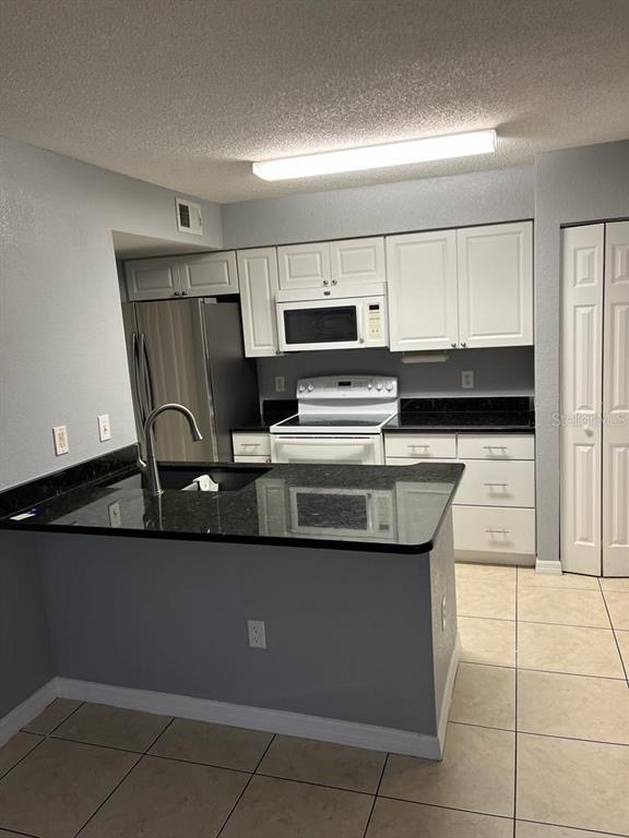 A kitchen features white cabinets, black countertops, stainless steel appliances, and light-colored tile flooring — 2207 ANTIGUA PLACE UNIT 715, KISSIMMEE, FL
