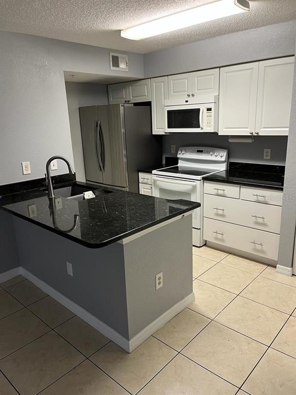 A kitchen features white cabinets, black countertops, stainless steel appliances, and light-colored tile flooring — 2207 ANTIGUA PLACE UNIT 715, KISSIMMEE, FL