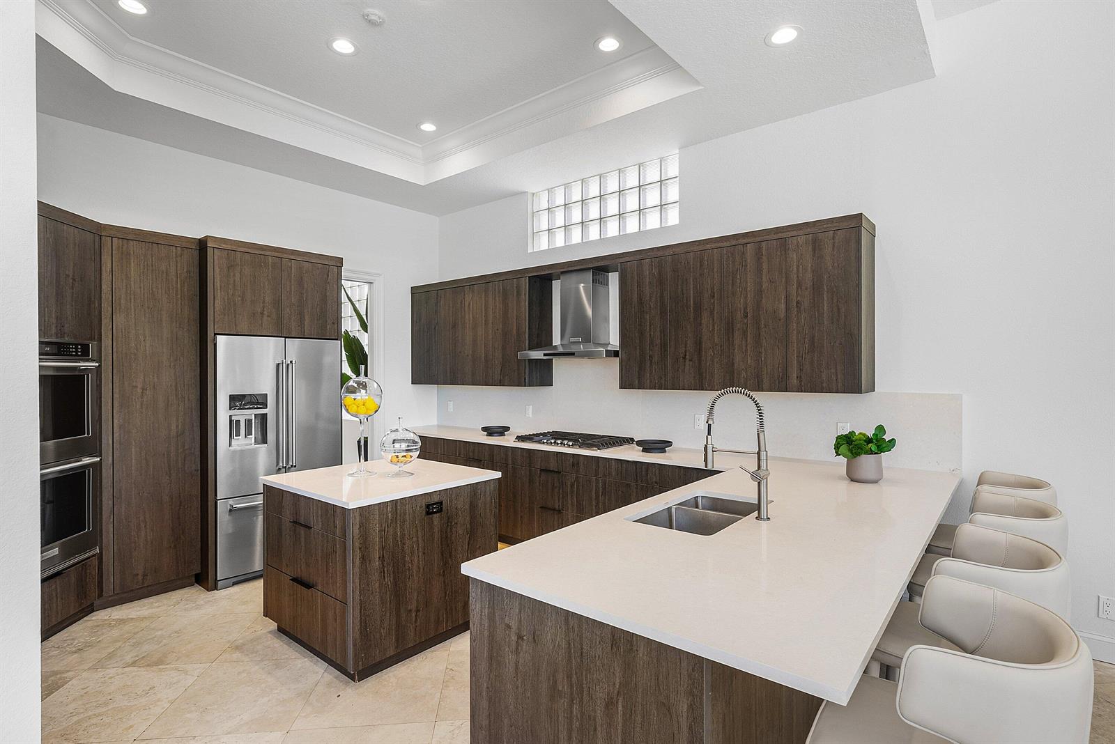 A modern kitchen features dark wood cabinetry, white quartz countertops, a central island, and stools — 16032 Bristol Isle Way, Delray Beach FL 33446, DELRAY BEACH, FL
