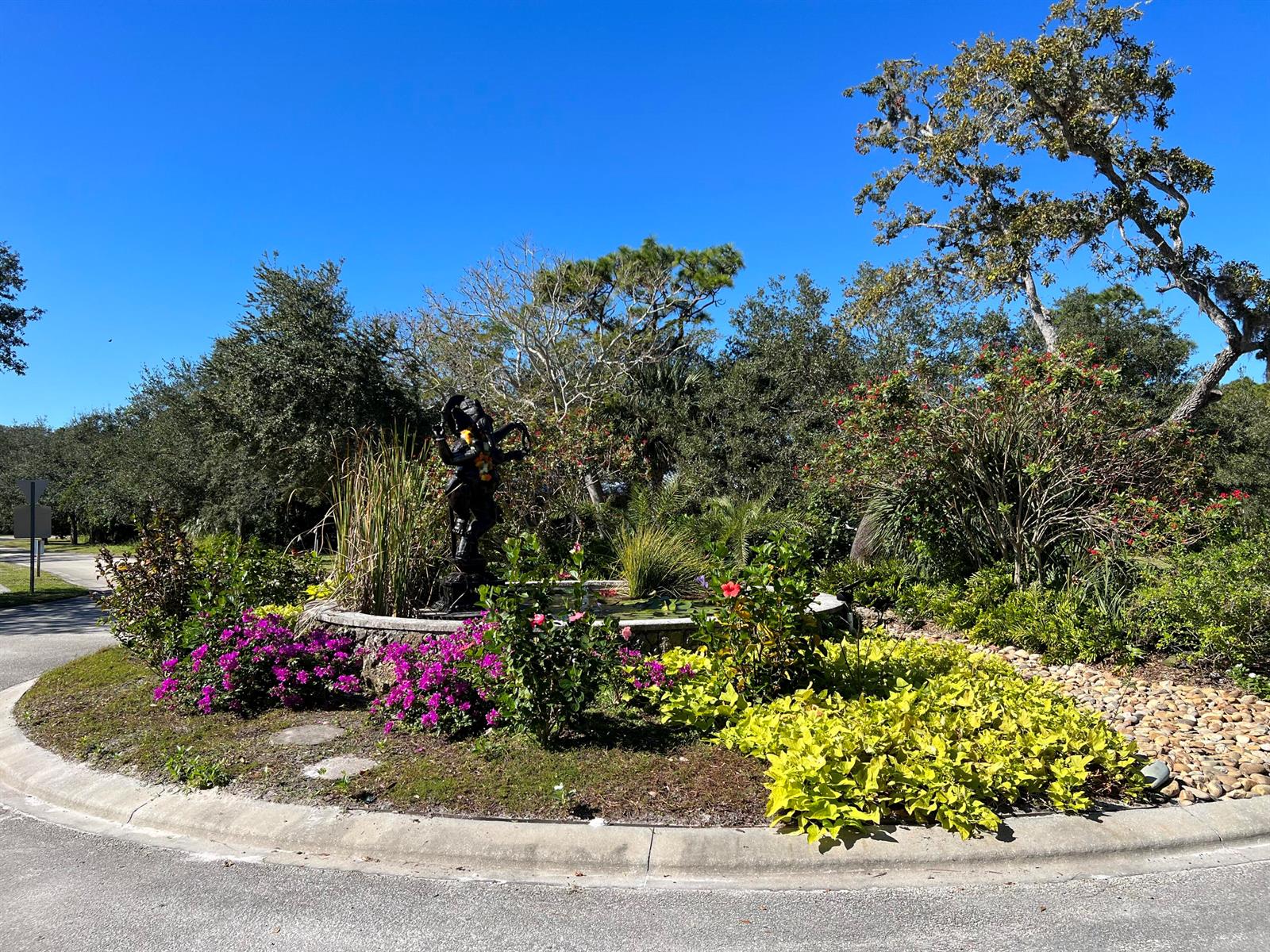 A circular garden bed features a central statue, colorful flowers, and lush landscaping — 11324 Ganesh Way, Sebastian FL 32958, SEBASTIAN, FL