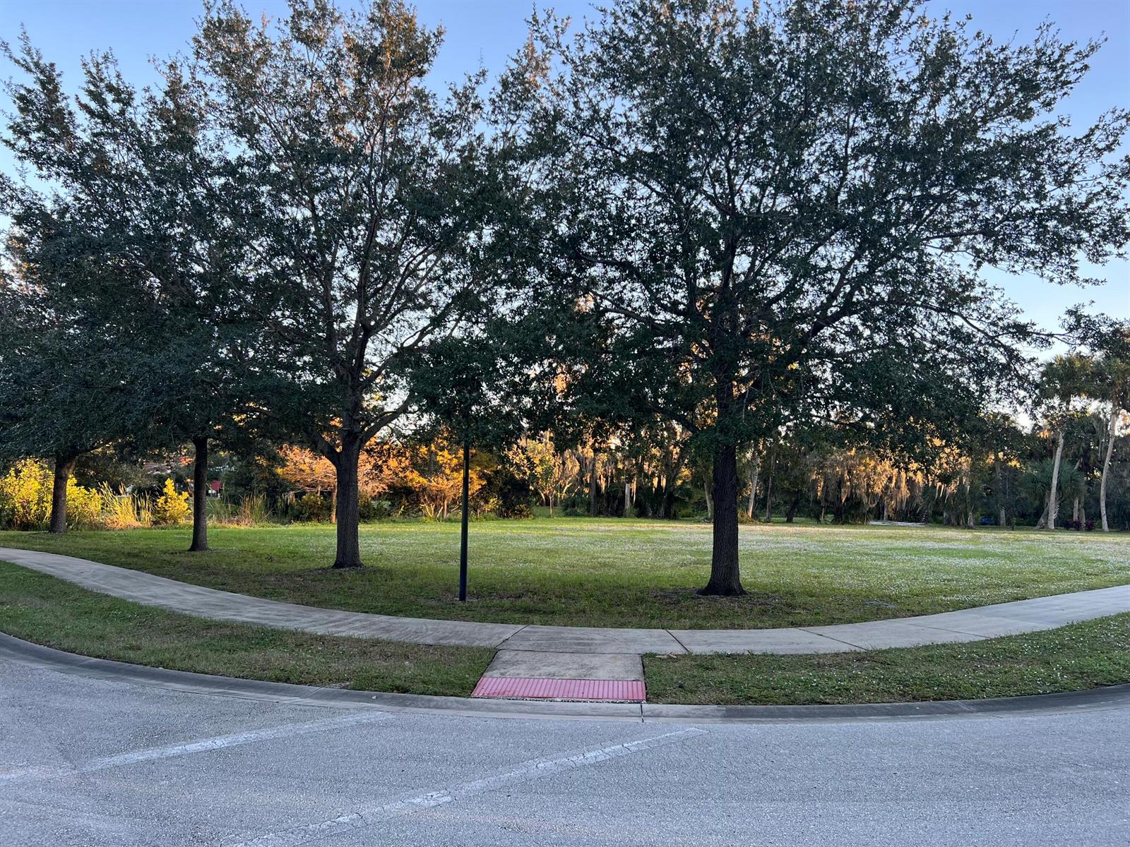 A grassy park area features three large trees and a curved concrete sidewalk — 11324 Ganesh Way, Sebastian FL 32958, SEBASTIAN, FL