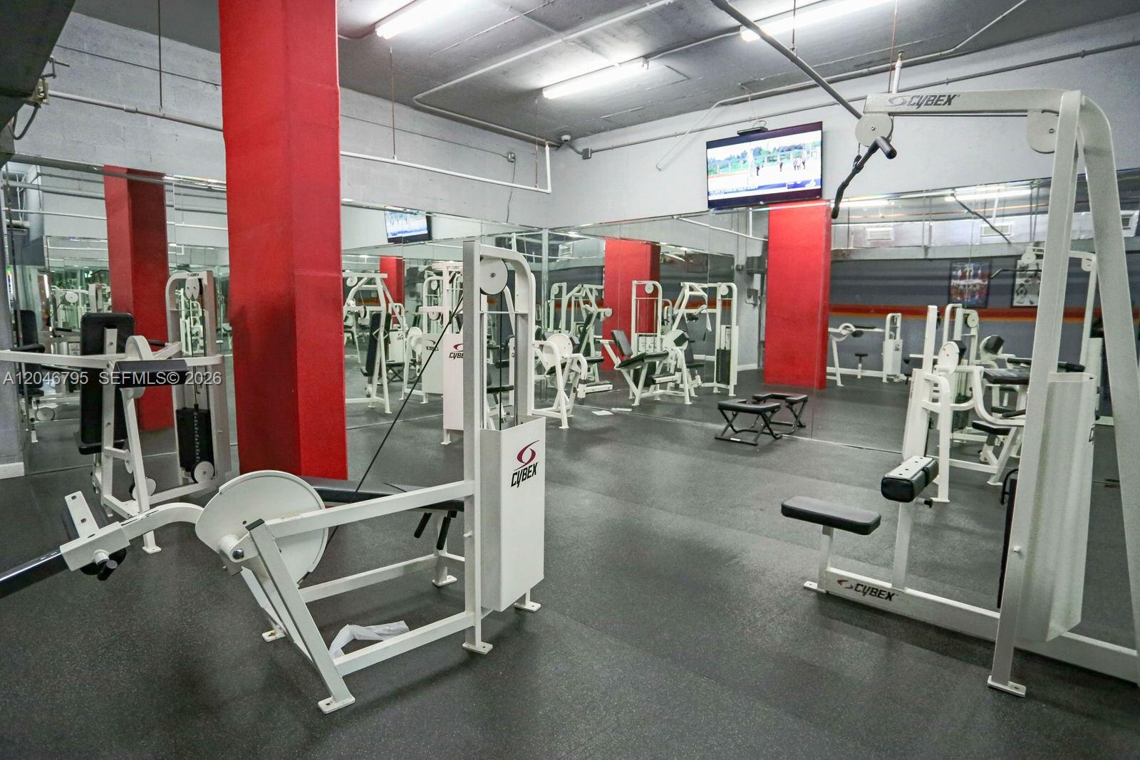 A gym room features white Cybex exercise equipment, mirrored walls, and red support pillars — 915 NW 1st Ave, Miami FL 33136, MIAMI, FL