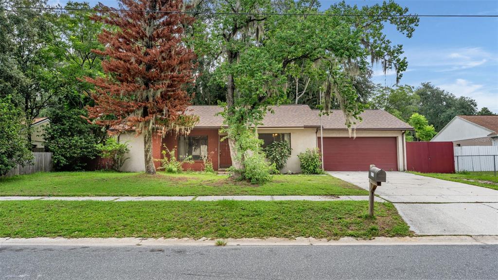 A single-story house with a red garage door, brick accents, and large trees in the yard — 2110 JOHNSON LOOP, PLANT CITY, FL