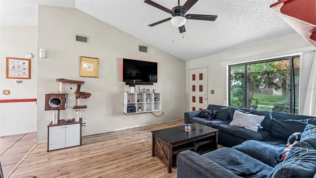 A living room features a vaulted ceiling, wood-look flooring, a wall-mounted television, and a sectional sofa — 2110 JOHNSON LOOP, PLANT CITY, FL