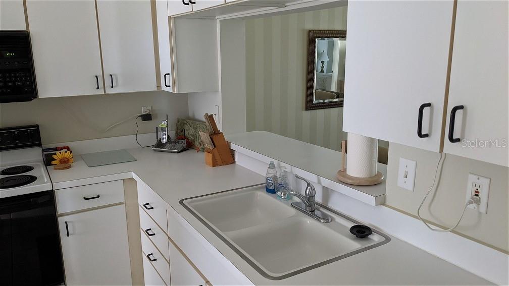 A kitchen features white cabinets, white countertops, a double-basin sink, and a pass-through window — 9300 CLUBSIDE CIRCLE UNIT 1306, SARASOTA, FL