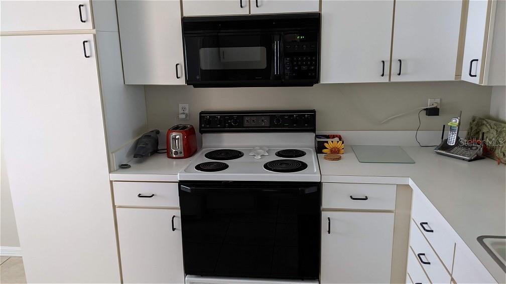 A kitchen features white cabinets, a black microwave, a white electric stove, and white countertops — 9300 CLUBSIDE CIRCLE UNIT 1306, SARASOTA, FL