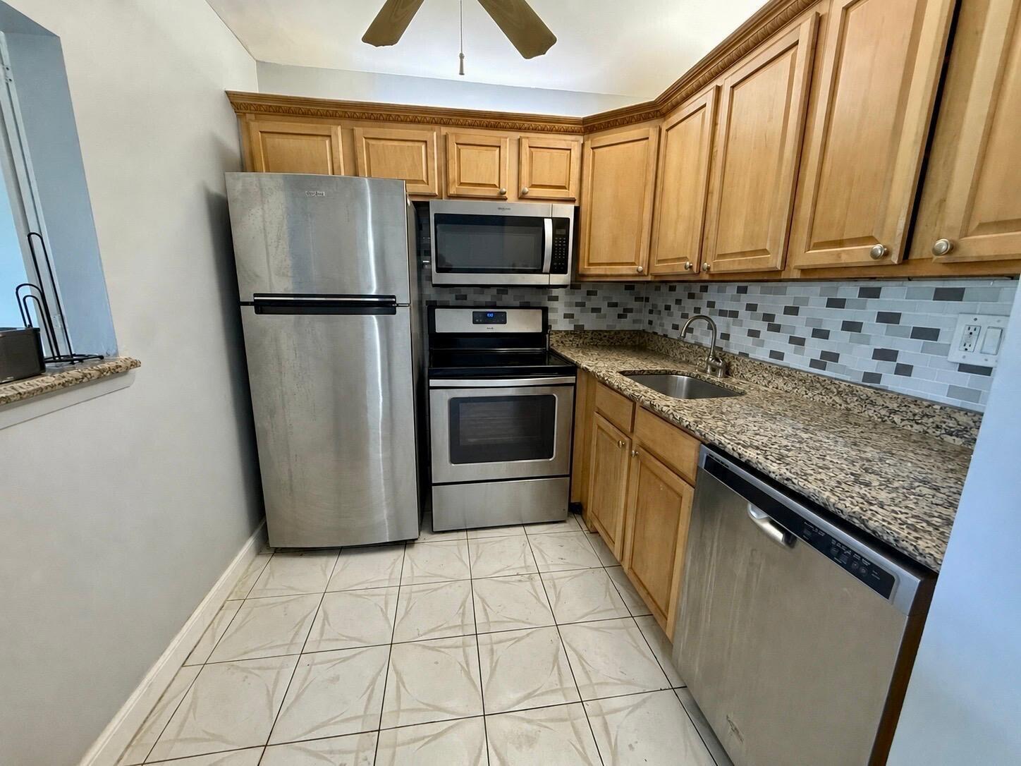 A kitchen features stainless steel appliances, light wood cabinets, granite countertops, and tiled flooring — 261 Suffolk, Boca Raton FL 33434, BOCA RATON, FL
