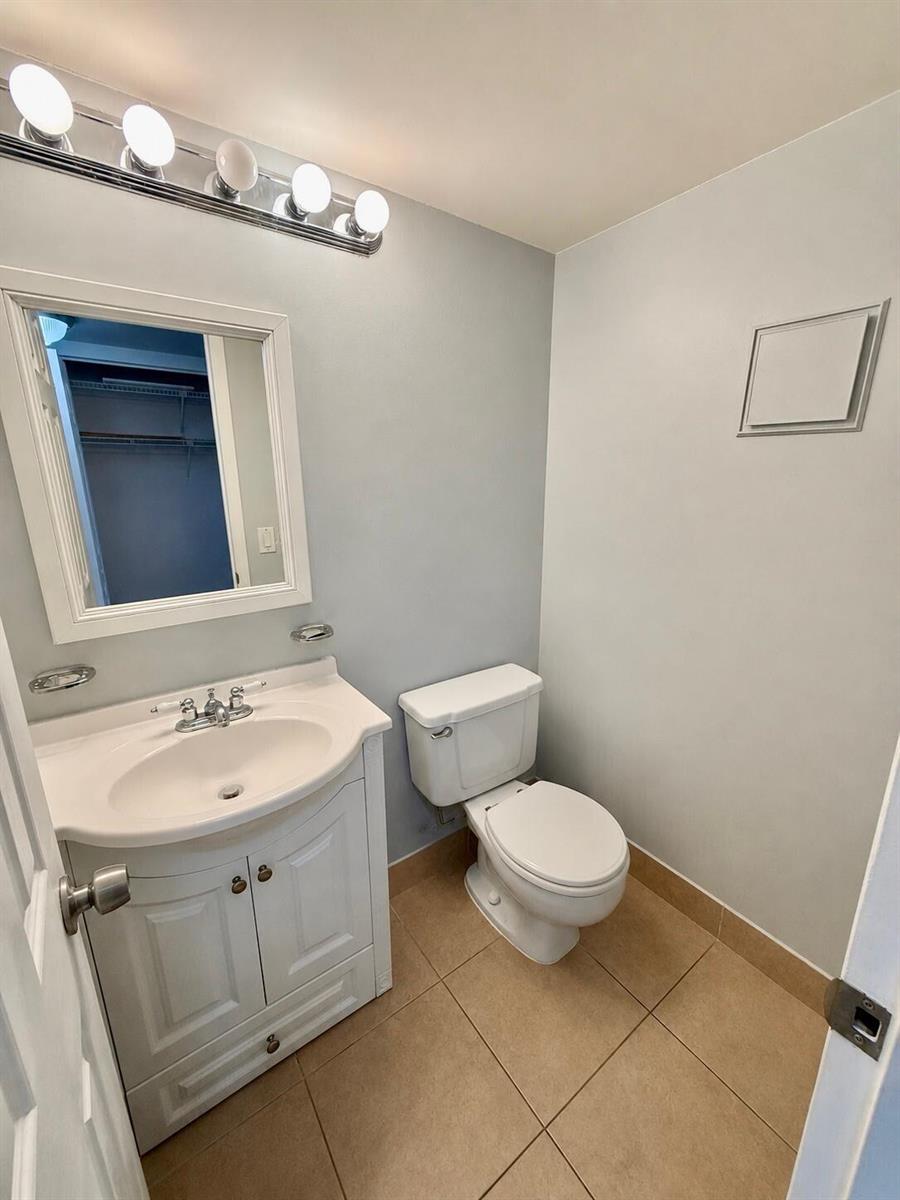 A small bathroom features a white vanity, a toilet, and light blue walls with tile flooring — 261 Suffolk, Boca Raton FL 33434, BOCA RATON, FL