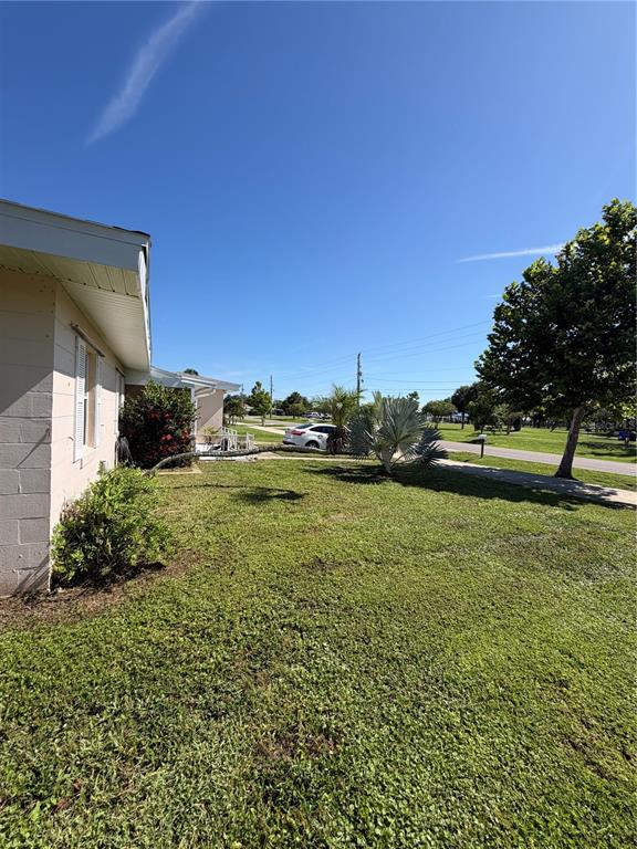 A view of a residential lawn with a house exterior, trees, and a parked car — 2353 ELKCAM BOULEVARD, PORT CHARLOTTE, FL