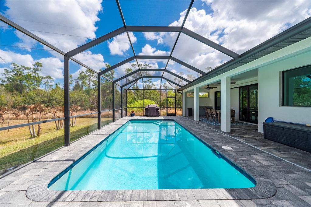 A rectangular swimming pool sits inside a screened-in lanai with stone pavers and outdoor furniture — 4301 SOUTH ROAD, NORTH FORT MYERS, FL