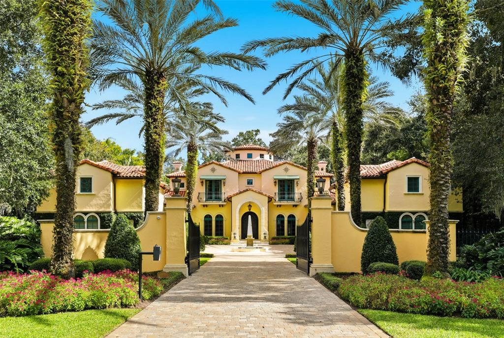 A yellow Mediterranean-style house with a gated driveway and tall palm trees in the front — 1120 PRESERVE POINT DRIVE, WINTER PARK, FL
