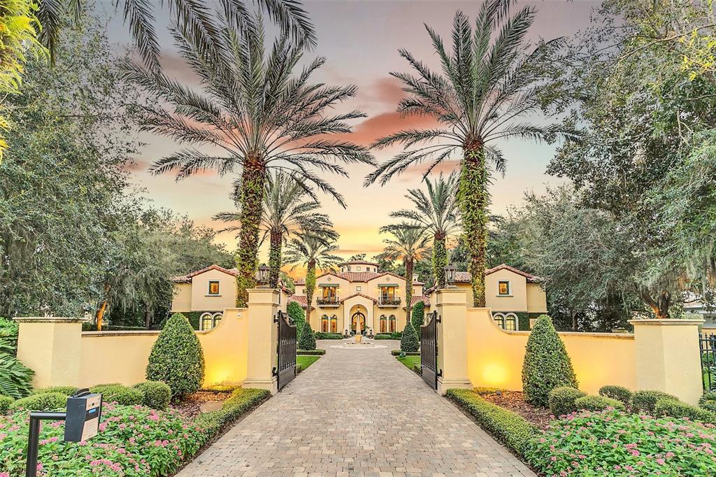 A paved driveway leads through a gated entrance toward a large Mediterranean-style house with palms — 1120 PRESERVE POINT DRIVE, WINTER PARK, FL