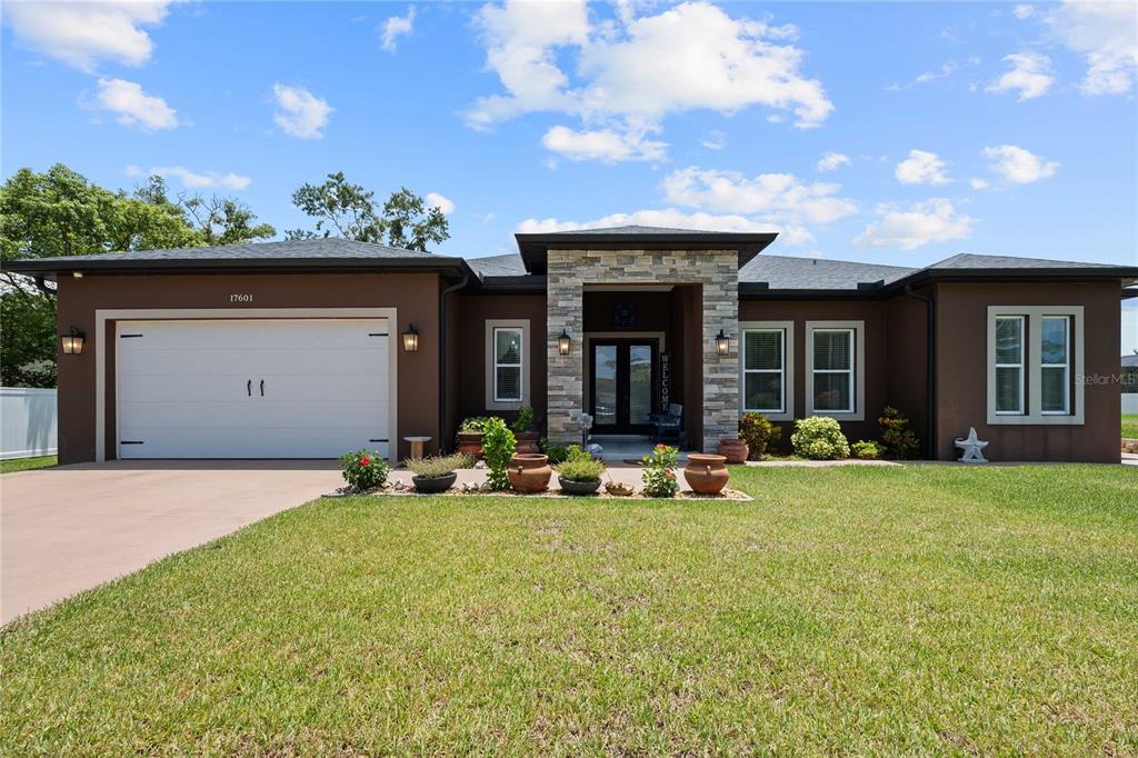 A single-story house with a brown stucco exterior, stone entryway, and a two-car garage — 17601 HANNA ROAD, LUTZ, FL