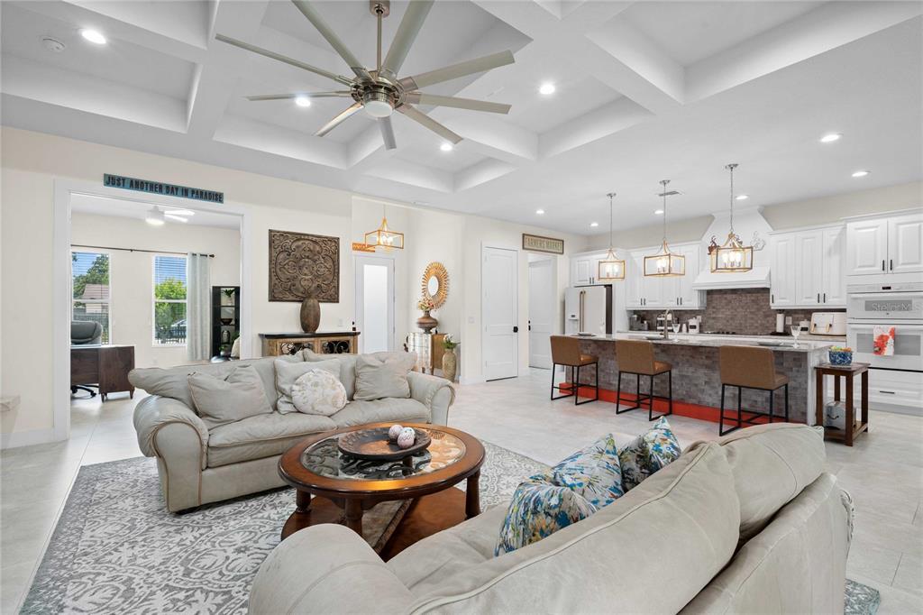 An open-concept living room and kitchen featuring a coffered ceiling, tile floors, and island seating — 17601 HANNA ROAD, LUTZ, FL