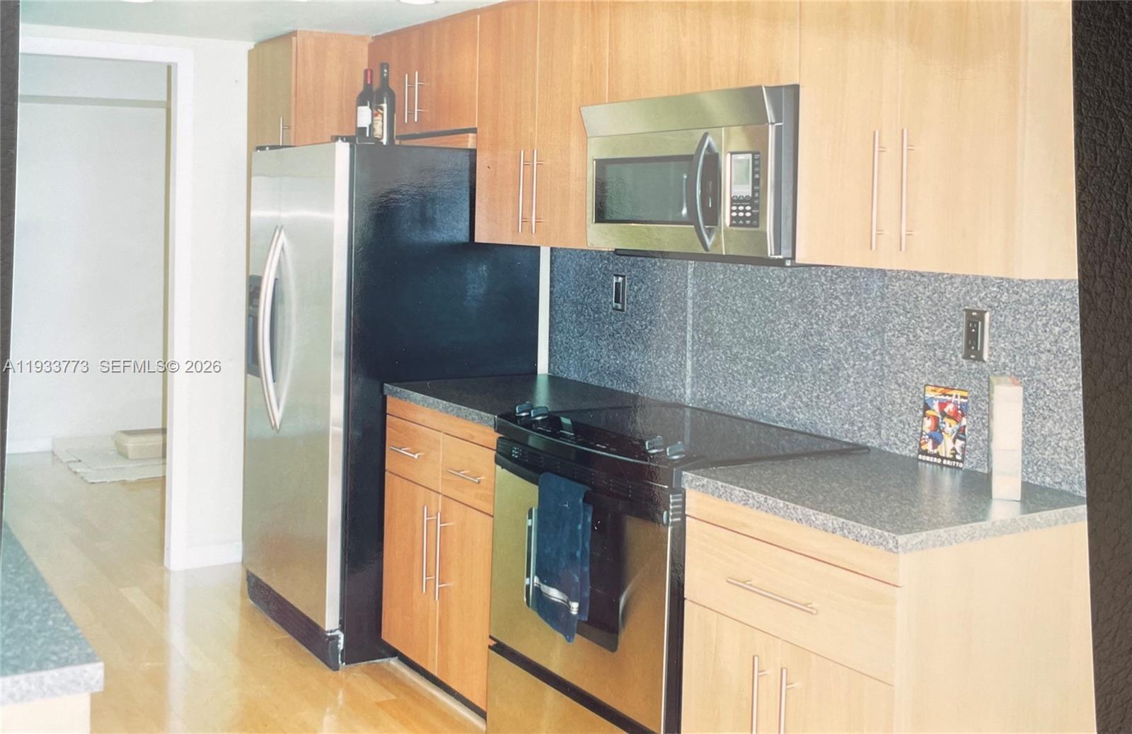A kitchen features light wood cabinets, stainless steel appliances, and dark gray countertops — 1000 Quayside Ter # 806, Miami FL 33138, MIAMI, FL