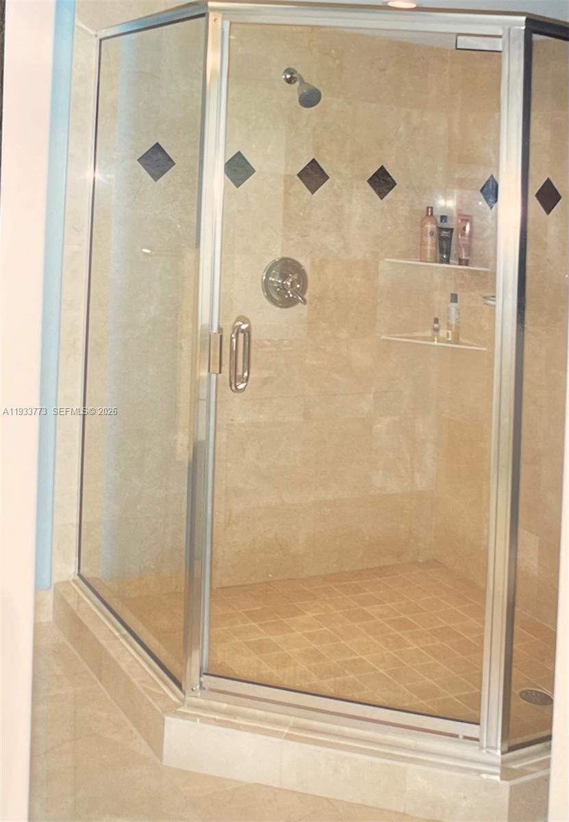 A corner glass shower stall features beige stone tile walls with decorative diamond-shaped accents — 1000 Quayside Ter # 806, Miami FL 33138, MIAMI, FL