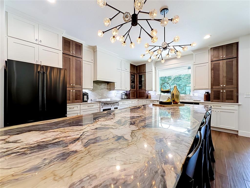 A kitchen features a large stone island, two modern chandeliers, and two-toned cabinetry — 4977 SW 1ST AVENUE, OCALA, FL