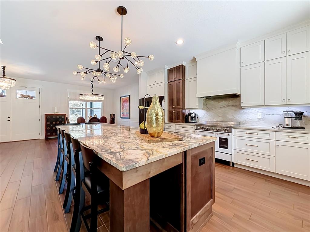 A kitchen features a large stone-topped island, white cabinetry, and a modern branching chandelier — 4977 SW 1ST AVENUE, OCALA, FL