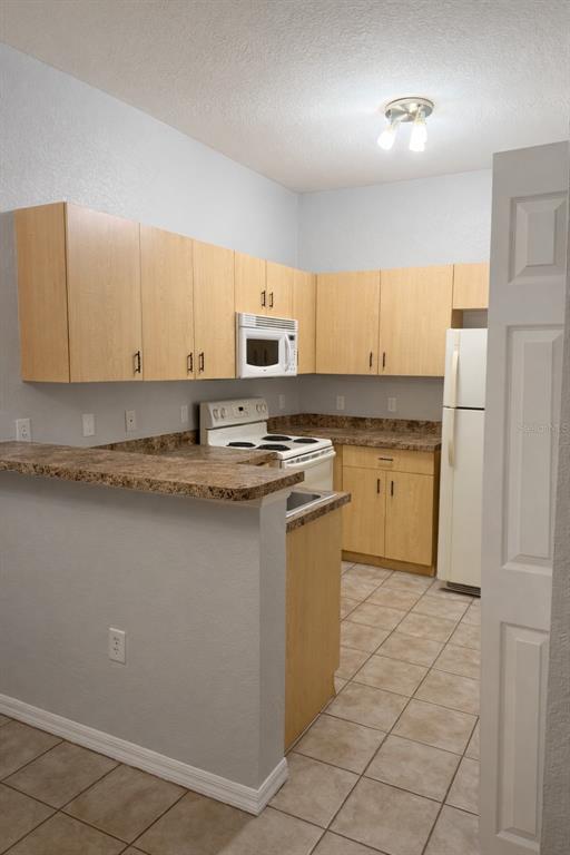 A kitchen features light wood cabinets, laminate countertops, white appliances, and beige tile flooring — 341 PORT PLEASANT DRIVE UNIT 341, KISSIMMEE, FL