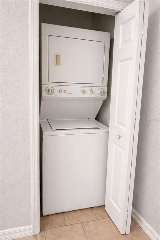 A white stacked washer and dryer unit sits inside a small closet with tiled flooring — 341 PORT PLEASANT DRIVE UNIT 341, KISSIMMEE, FL
